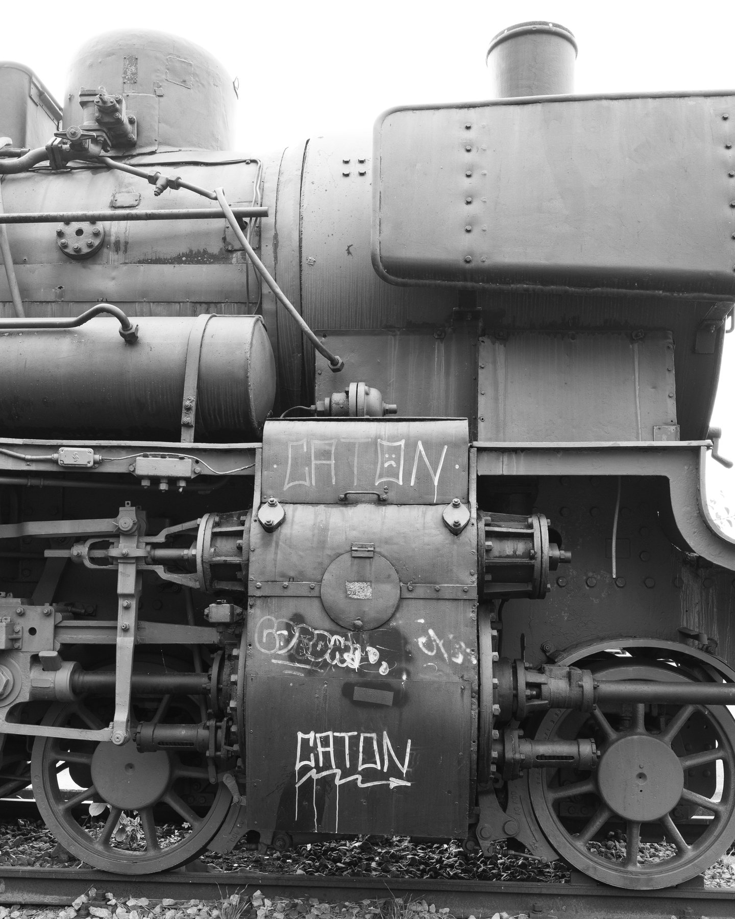 side view of a steam locomotive's wheels and boiler marked with graffiti, black and white
