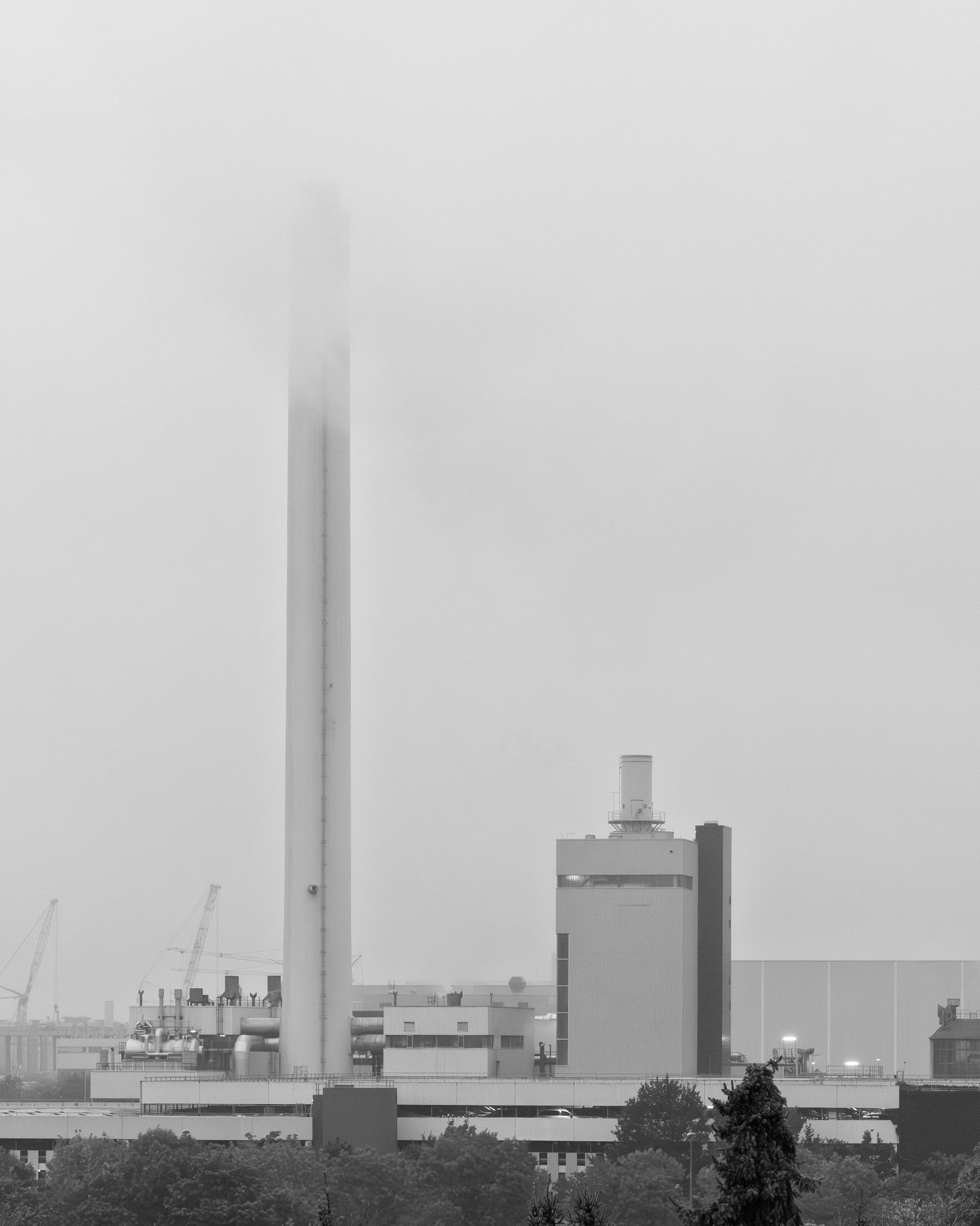 tall industrial chimney vanishing into low fog above a power plant under an overcast sky