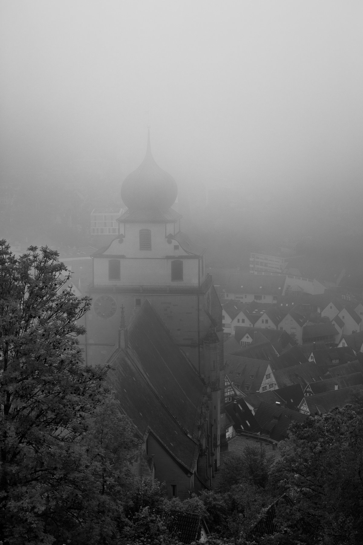 church tower with onion dome rising above village rooftops in dense fog