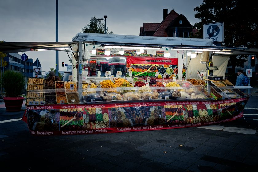 brightly lit dried-fruit market stall on a darkening city street corner at dusk