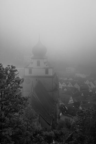 church tower with onion dome rising above village rooftops in dense fog